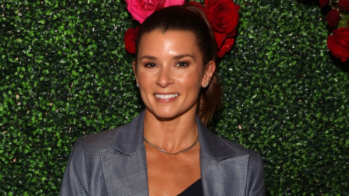 Danica Patrick poses in front of a green background in a gray plaid blazer and silver necklace.